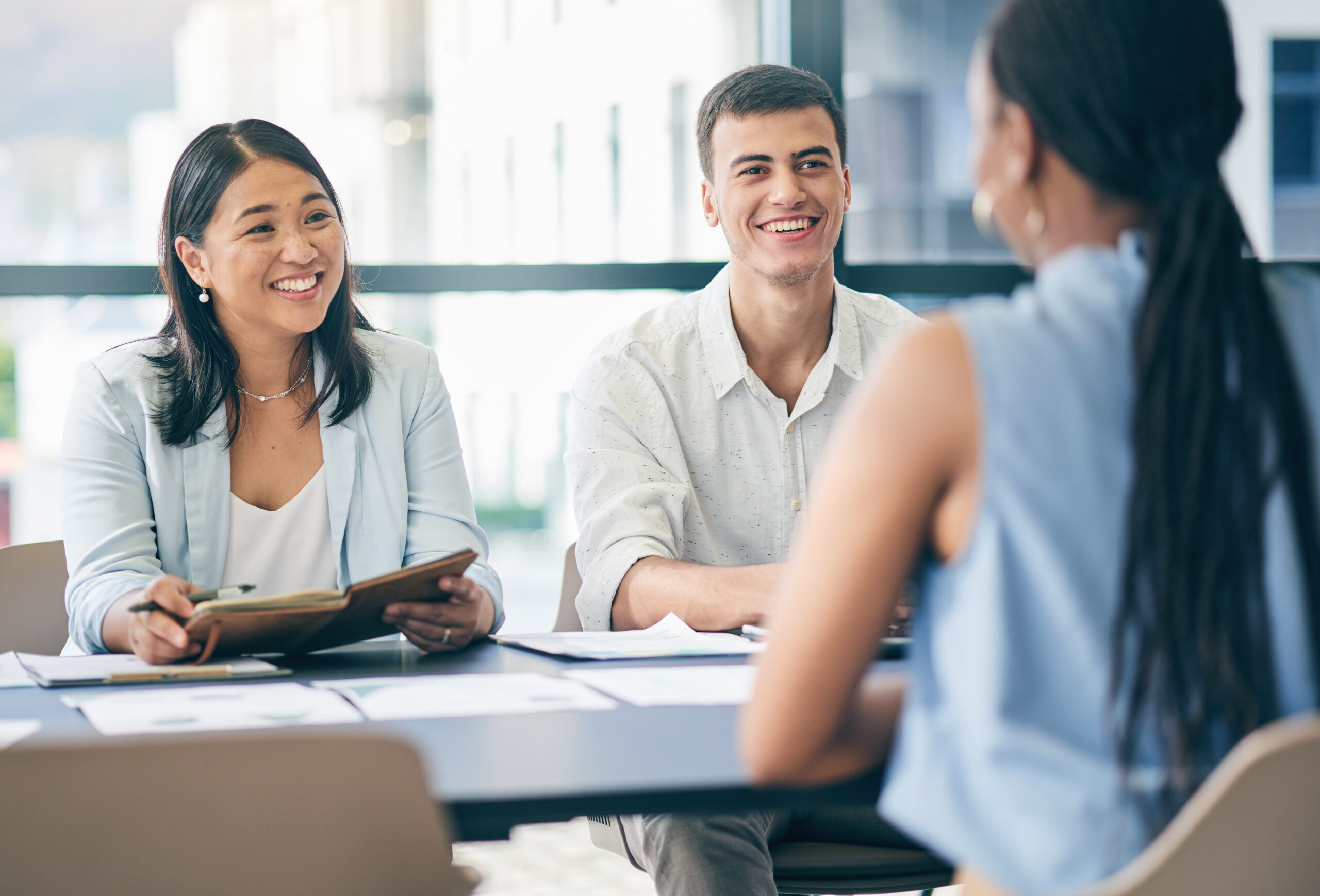 Two hiring managers interviewing a job applicant in a bright, modern office setting.